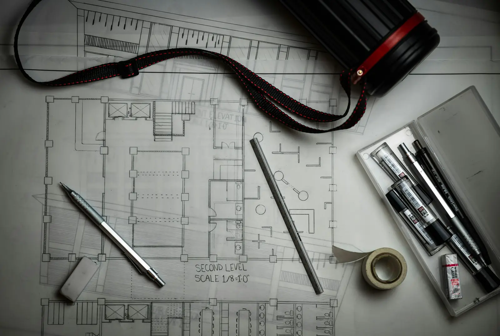 Architectural drawings with pencils, a metal ruler and a drawing tube