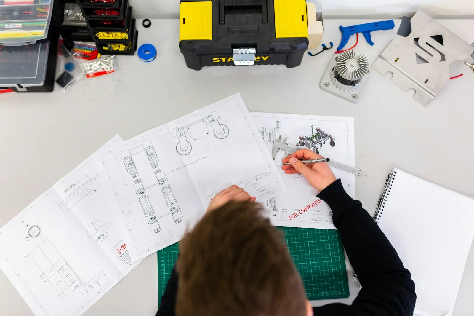 Overhead view of technical drawings being reviewed at a desk with a toolbox