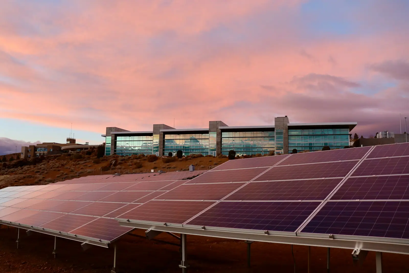 Rooftop solar panel array beside a low building at sunset
